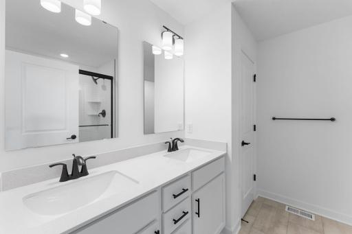 A quartz-topped vanity with dual sinks and individual mirrors optimize shared living, while a glass-enclosed shower promotes timely morning rituals