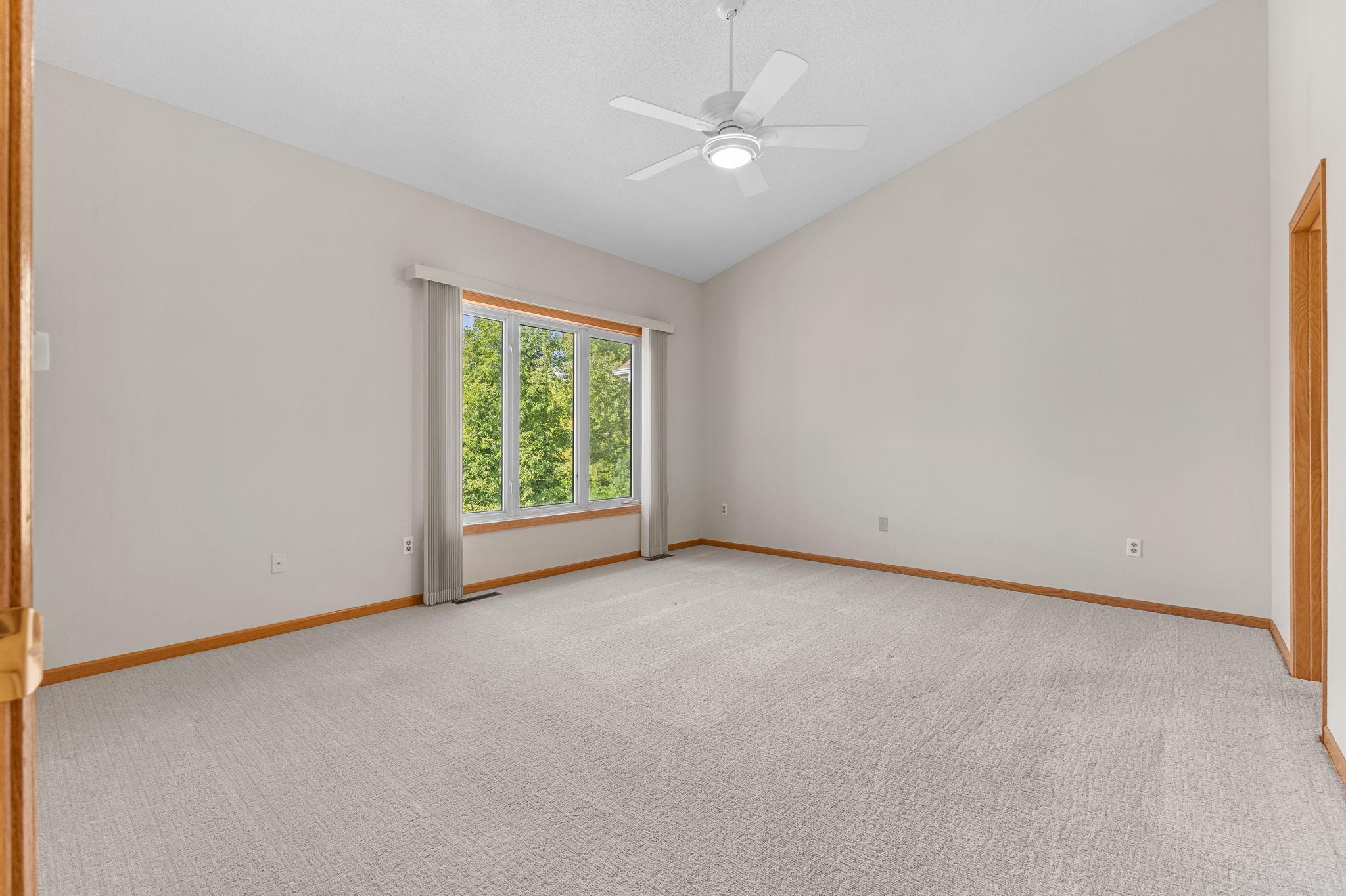 Generous primary bedroom with plush carpeting, vaulted ceilings, abundant natural light, and a ceiling fan for added comfort.