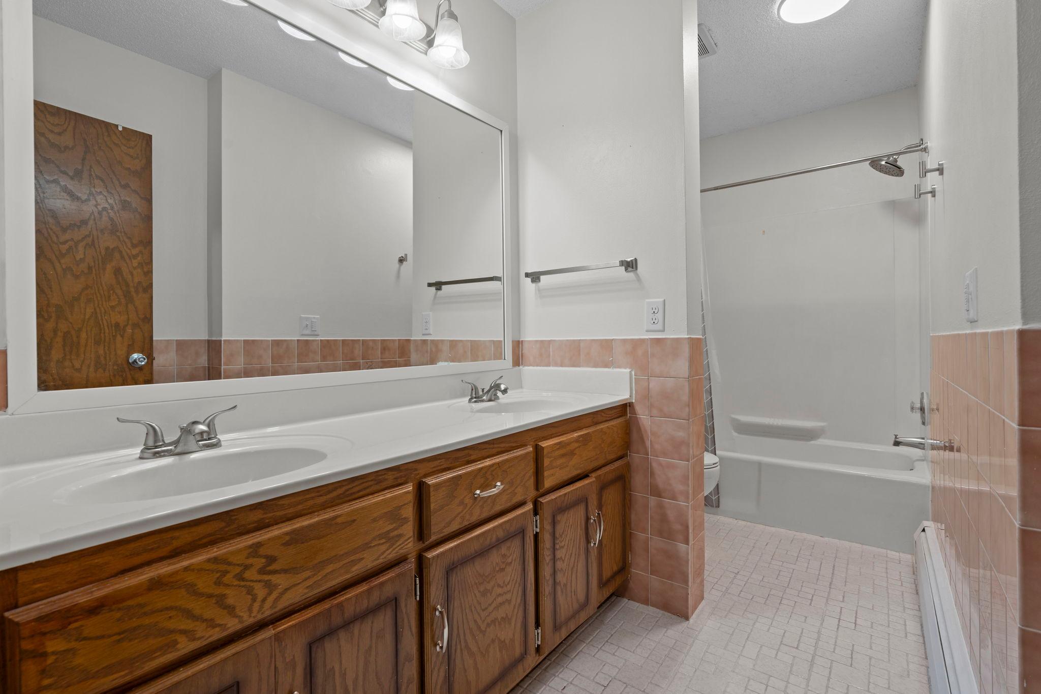 The nearby full bathroom features tile flooring, a dual vanity, and a tub/shower combination.