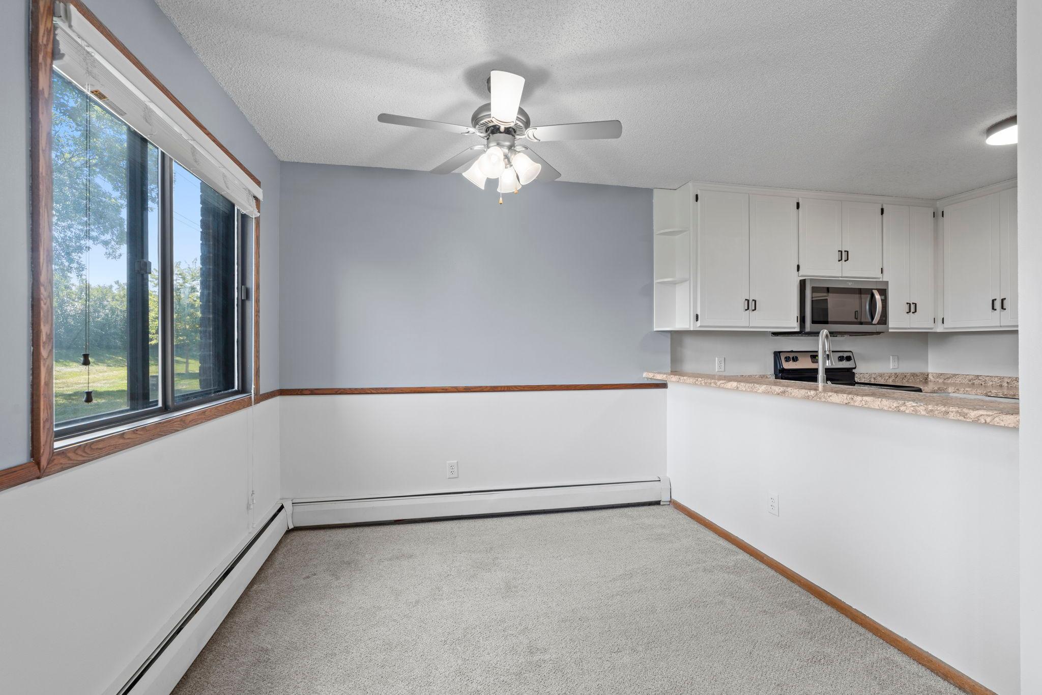 The adjacent dining area offers carpeting, a ceiling fan, and a large window that fills the space with natural light.