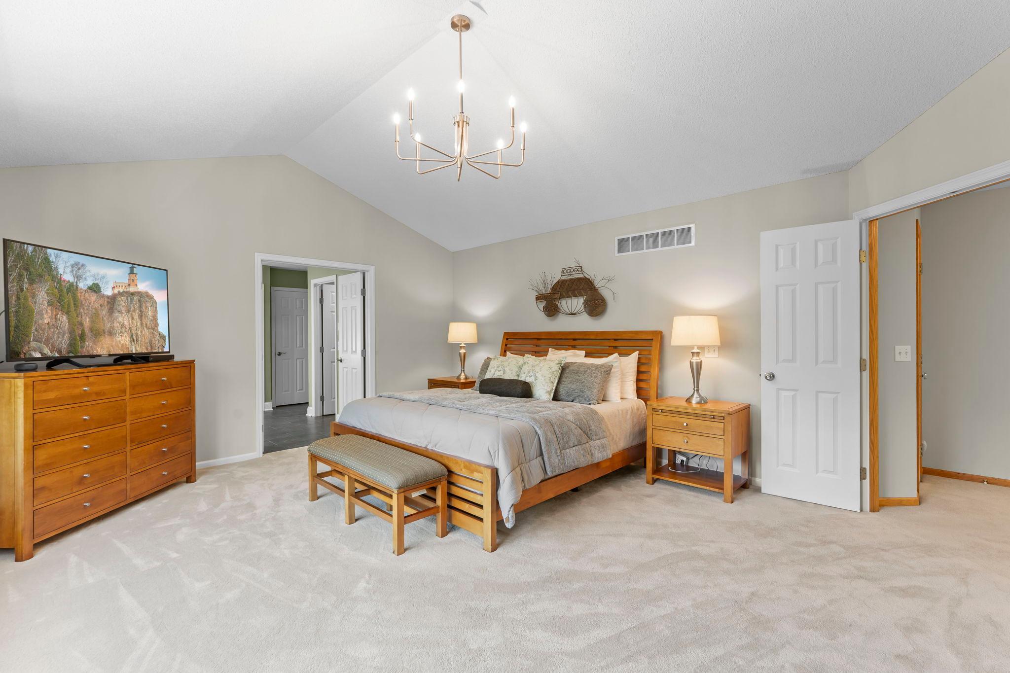 The spacious primary bedroom features soaring 10-foot vaulted ceilings, new carpeting, a stylish modern chandelier, and a large rear-facing window.