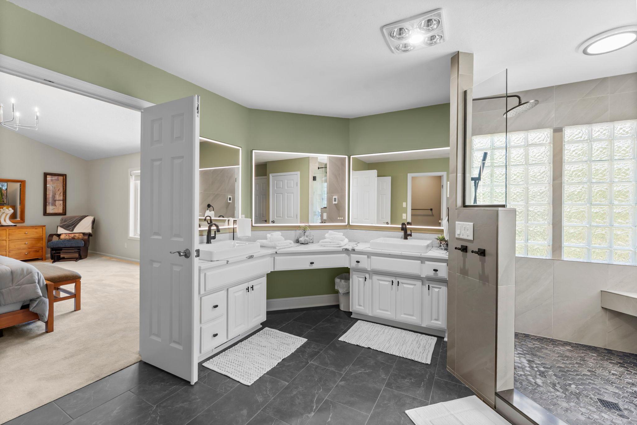 Double doors lead to the private ensuite with oversized dual marble vanities, illuminated mirrors, a luxurious 6x5 tiled walk-in shower, separate water closet, and access to a stacked LG washer/dryer near the expansive 12x9 walk-in closet.