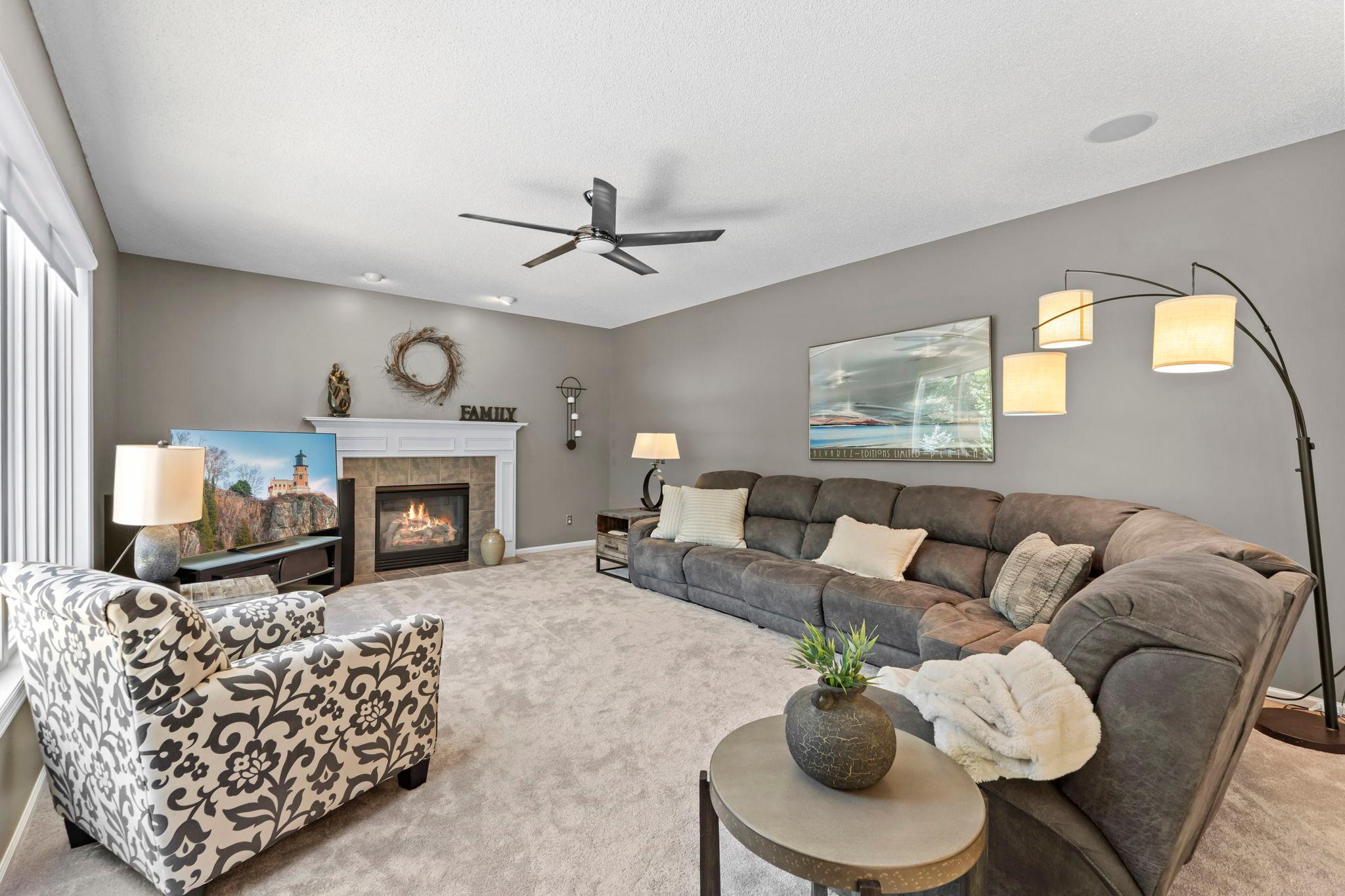 The generously sized main-level living room offers brand-new carpeting, a ceiling fan, cozy gas fireplace, and large windows that create a bright and inviting atmosphere.