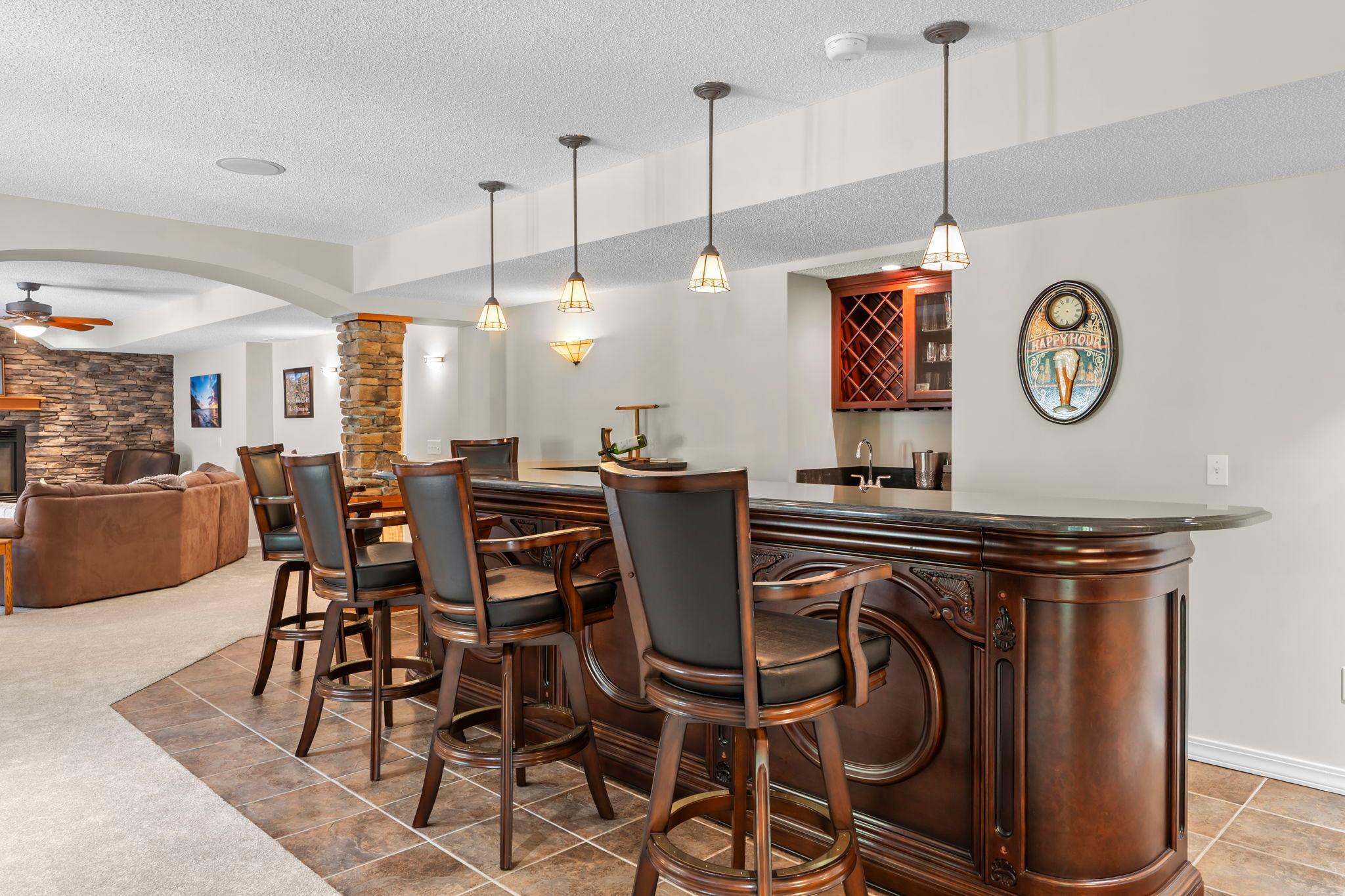 The impressive wet bar features bar seating, tile flooring, pendant lighting, sink, beverage refrigerators, and wine storage.