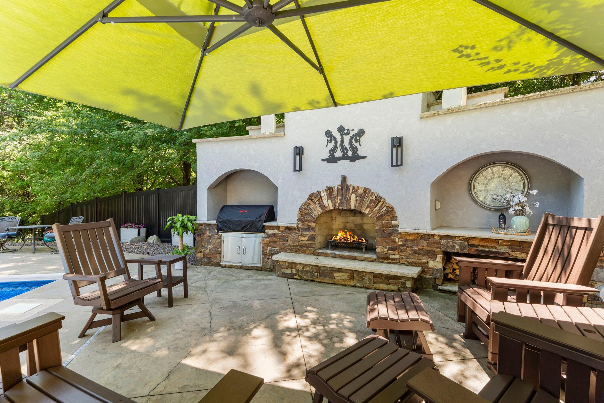 An additional outdoor patio area features a wood-burning fireplace with built-in grill, creating the perfect space for summer gatherings and memorable evenings outdoors.