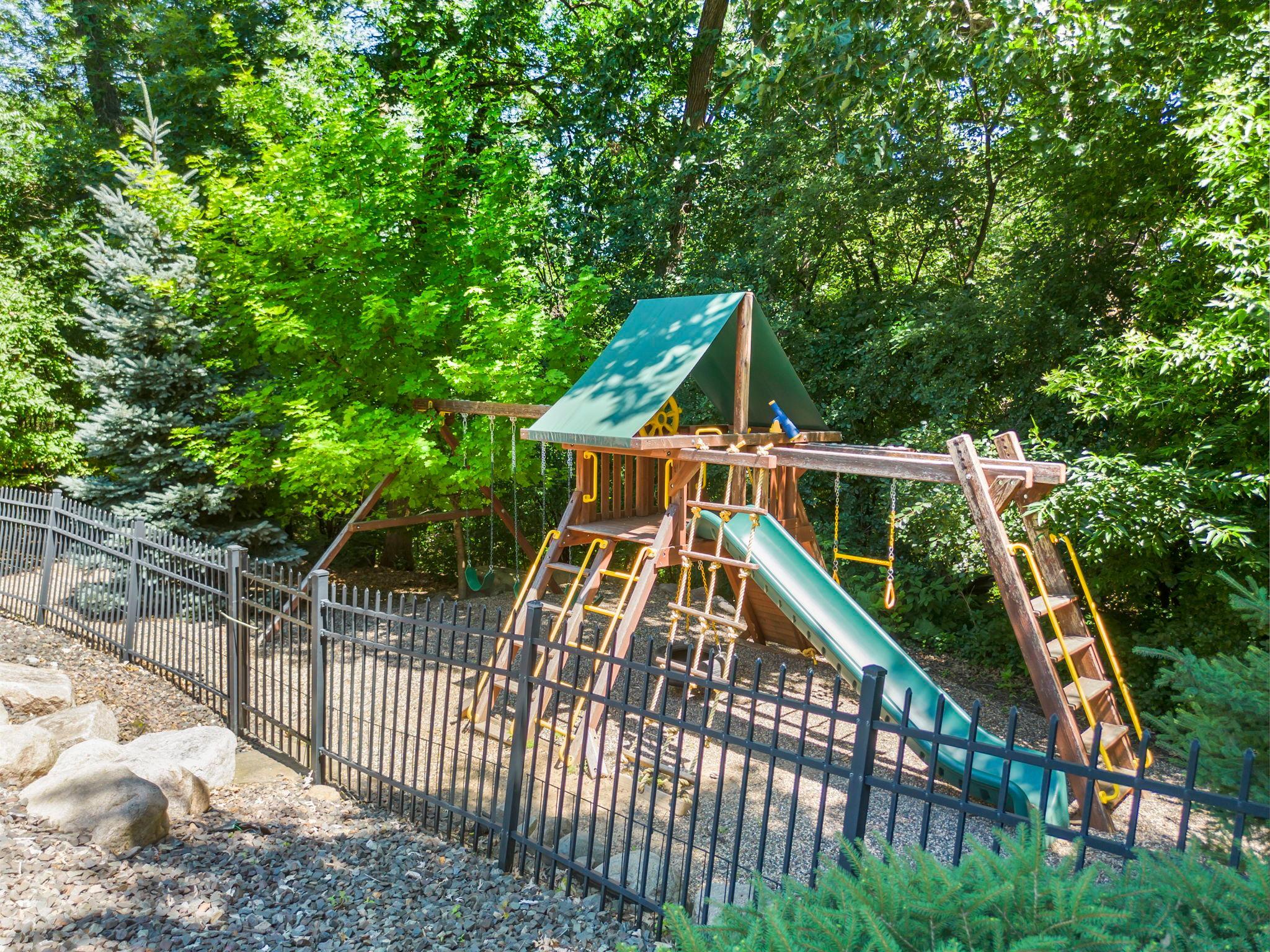 Beyond the fenced yard, a gravel play area with playset provides additional space for recreation.
