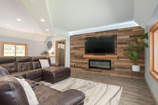Remodeled Recreation Room offering a wooden accent wall with an electric fireplace, bar area with refrigerator, game area, and custom cabinetry