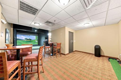 Golf simulator with pub chairs, putting green, and storage lockers.
