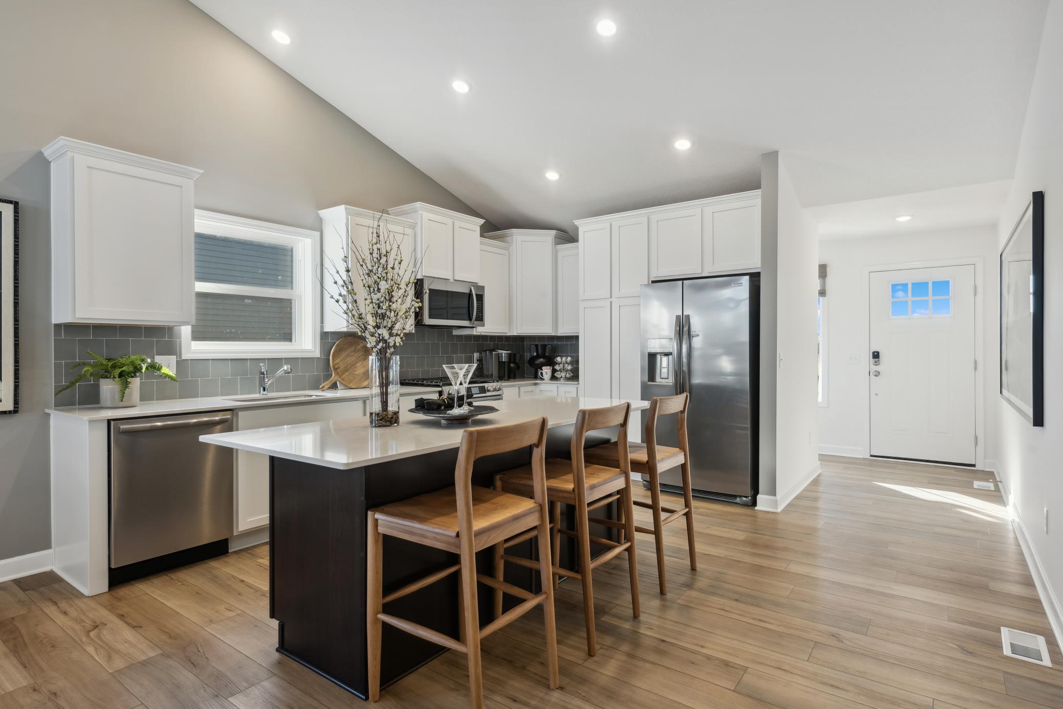(Photo of a decorated model, actual homes finishes will vary) This spacious kitchen features a large center island, quartz countertops, LVP floors, stainless appliances and more!