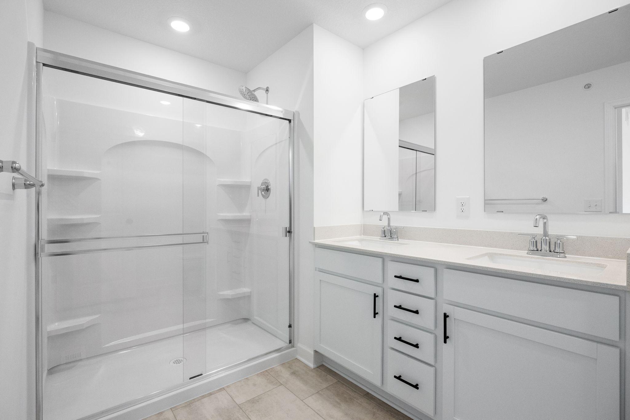 Featuring a glass-enclosed shower with built-in shelving and glass mirrors set atop dual quartz sinks and vanity-cabinetry, the en-suite bathroom helps streamline morning routines