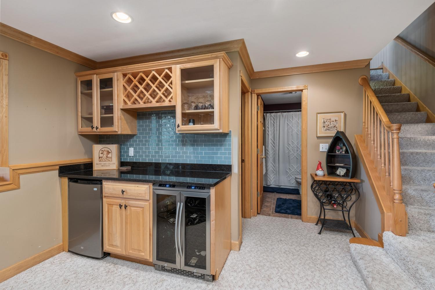 This nice little corner bar features display cabinetry with wine rack, granite counter top, subway tile, beverage fridge and wine cooler.