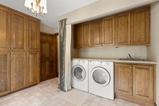 The laundry room, which features backyard views and easy access to the mudroom, with a wall of cabinetry for storage, countertops, as well as a sink.
