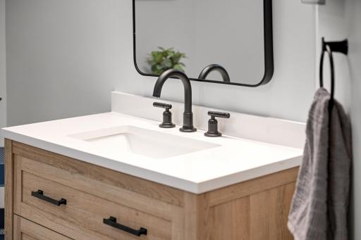 Attractive wood-tone vanity with a bright solid-surface top, undermount sink, and contemporary matte-black fixtures.