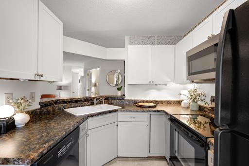 Efficient kitchen layout with white cabinetry, abundant workspace, and a combination of black and stainless-finish appliances.