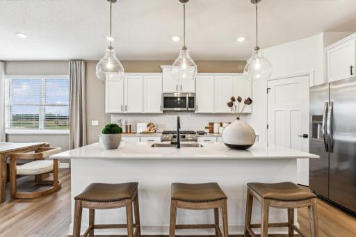 (Photo of a decorated model, actual homes finishes will vary) The stunning kitchen features a large center island, quartz countertops, LVP floors, stainless appliances and more!