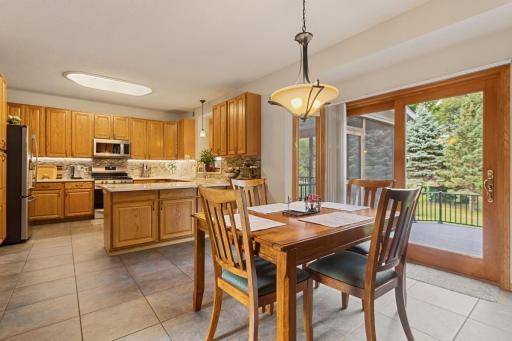 The informal dining area features porcelain tile that flows seamlessly into the kitchen, with a convenient snack bar seating ledge and breakfast area. A sliding door opens to the deck and screened porch, surrounded by the beautiful backyard trees.
