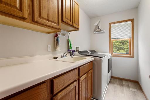 Nicely finished laundry room with beautiful plank flooring, full-size washer and dryer, laundry tub, and abundant cabinet storage. A window brings in natural light, making laundry day a little brighter.