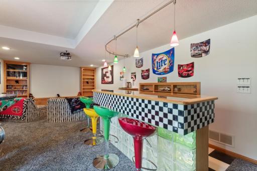 NASCAR fan’s dream! This ultimate man cave features a custom-built bar with glass enclosure and miniature racetrack, built-in bottle shelving and colorful pendant lights—perfect for entertaining and race-day fun!