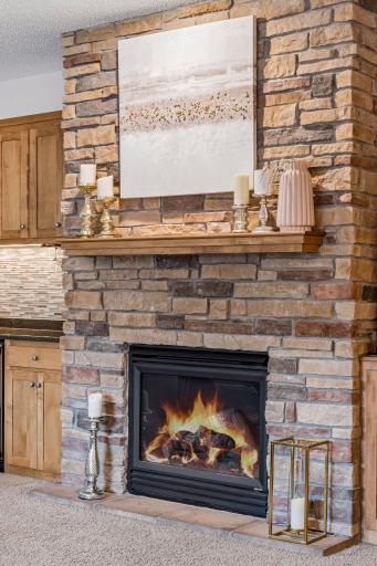 Gas fireplace in the living room with floor-to-ceiling stonework and maple mantle.