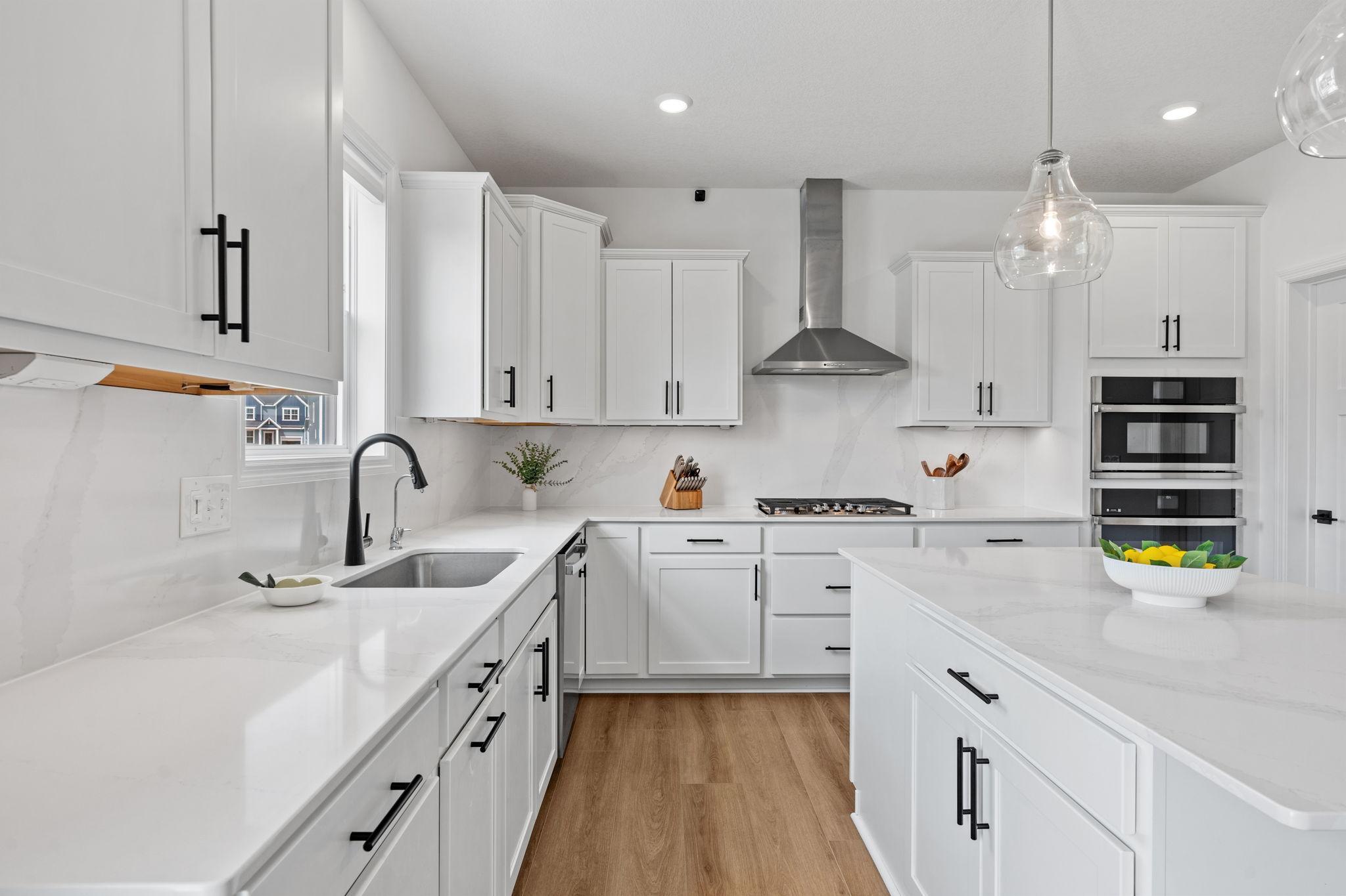 Gourmet Kitchen w/ white cabinetry, center island, quartz counters + backsplash, SS undermount sink, upgraded GE Smart Profile apps incl gas cooktop, SS hood & walk-in pantry.