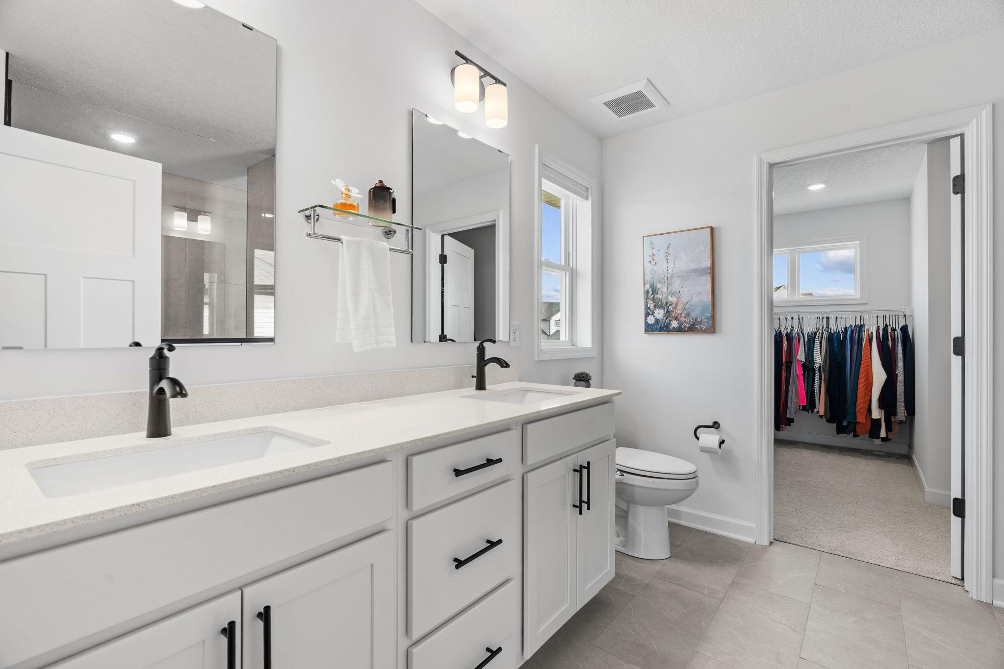 Primary Ensuite featuring dual sinks, quartz counters, upgraded Serenity Shower w/ floor-to-ceiling tile + dual shower heads & walk-in closet.