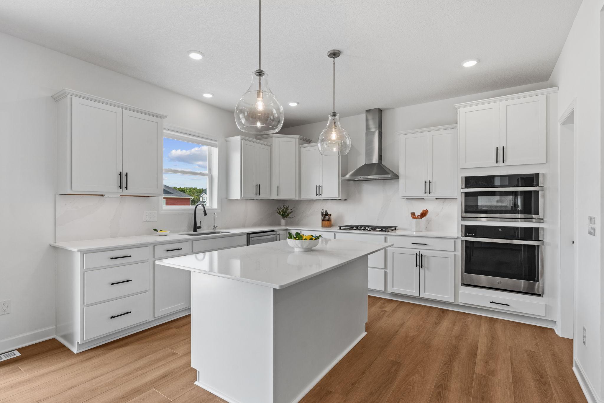 Gourmet Kitchen w/ white cabinetry, center island, quartz counters + backsplash, SS undermount sink, upgraded GE Smart Profile apps incl gas cooktop, SS hood & walk-in pantry.