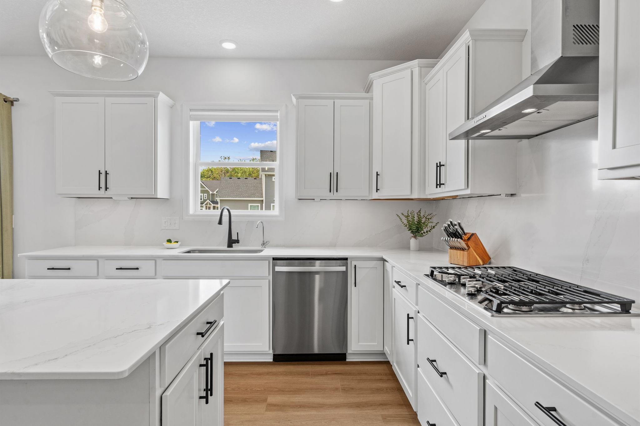 Gourmet Kitchen w/ white cabinetry, center island, quartz counters + backsplash, SS undermount sink, upgraded GE Smart Profile apps incl gas cooktop, SS hood & walk-in pantry.