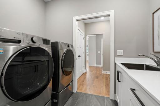 Convenient main level laundry room with front loading washer and dryer, laundry sink, cabinetry and additional storage.
