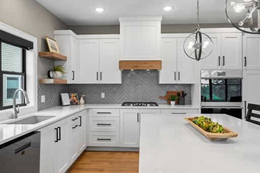 Stylish kitchen with white cabinetry, decorative backsplash, gas cooktop, wood accent range hood and open shelving.