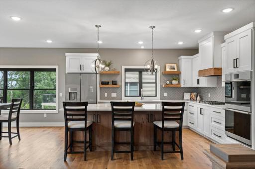 Spacious updated kitchen with white cabinetry, center island, breakfast bar, open shelving and modern finishes.