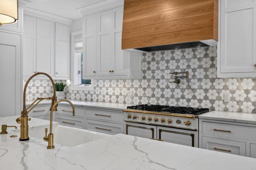 Quartz countertops with a decorative marble tile backsplash and enameled cast iron farmhouse sink. High-end appliances include 43" La Cornue gas range w/ pot filler and decorative white oak paneled hood.