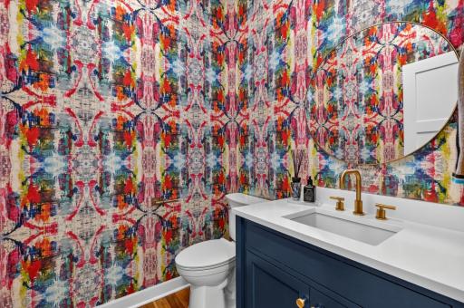 1/2 bathroom on the main level features decorative wall coverings and an enameled vanity cabinet, quartz top and wide spread faucet