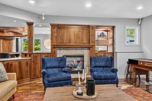 Family Room features 2-sided fireplace w/ stone tiled surround ad hearth. Custom walnut cabinetry, open display shelving with accent lighting, additional storage cabinet with quartz top, paneled fireplace surround and mantel