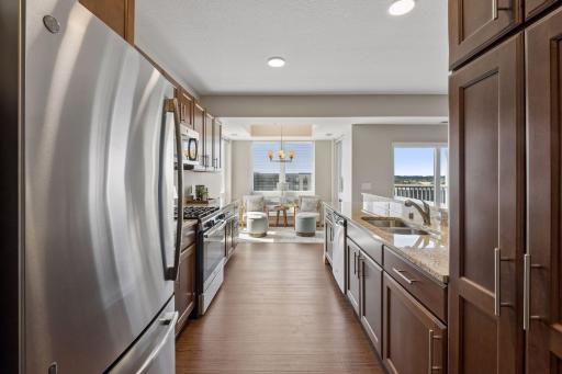 Modern galley style kitchen offering granite counters, SS appliances, hazelnut finished soft close cabinetry + gleaming luxury vinyl plank flooring.