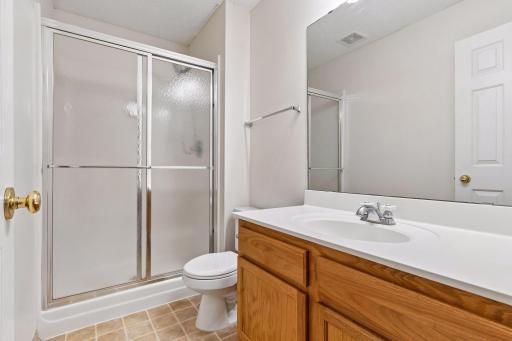 Finished lower-level full bath featuring an oak vanity, neutral tile flooring, and a walk-in shower stall with sliding glass doors.