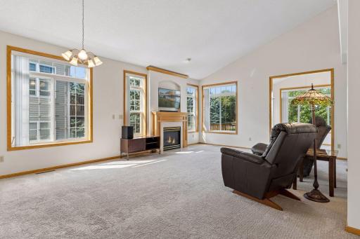 Bright and open main-level living room highlighted by soaring vaulted ceilings, large picture windows, and an electric fireplace with a custom mantle.