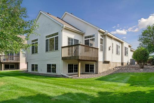 Low-maintenance vinyl exterior featuring an elevated deck off the main-level sunroom and large lower-level lookout windows surrounded by manicured HOA-maintained lawn.
