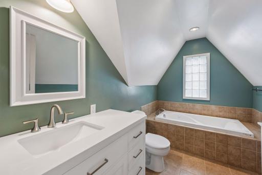 Primary bath features jetted tub all newer vanity sink, faucet, toilet, tile and glass block window.