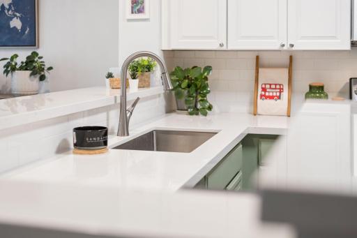Stainless-steel undermount sink with pull-down faucet surrounded by expansive white countertops and subway tile backsplash.