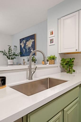 Close-up of the spacious undermount sink, modern pull-down faucet, white countertops, and distinctive sage-green cabinetry.