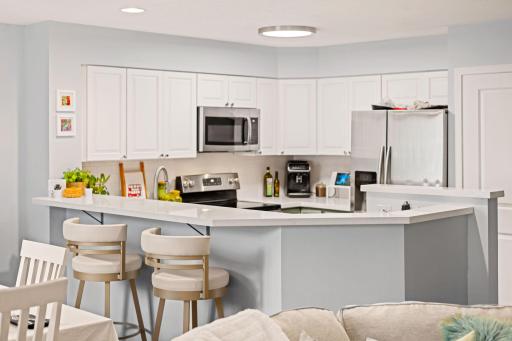 Open kitchen with white cabinetry, stainless-steel appliances, generous counter space, and an extended breakfast bar.