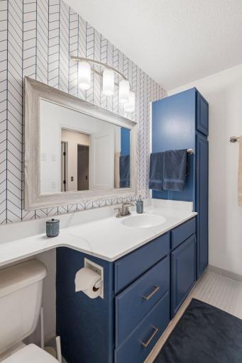 Stylish blue vanity with generous storage, bright countertop, updated lighting, and coordinating geometric accent wall.