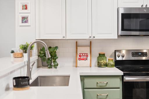 White upper cabinetry, subway tile backsplash, stainless-steel appliances, and contrasting sage-green lower cabinetry add character to the kitchen.