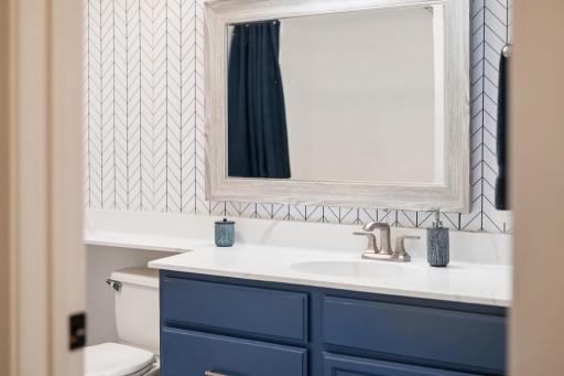 Updated bathroom detail featuring a blue vanity, bright countertop, framed mirror, and stylish geometric accent wall.