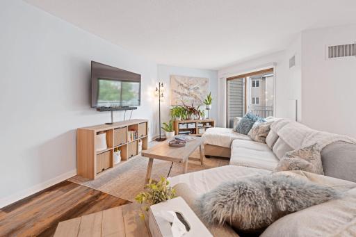 Generously sized living room with a large sectional, natural light, and direct access to the private balcony.
