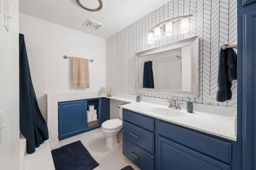 Spacious full bathroom featuring generous vanity storage, updated finishes, accent wall, and tub/shower combination.