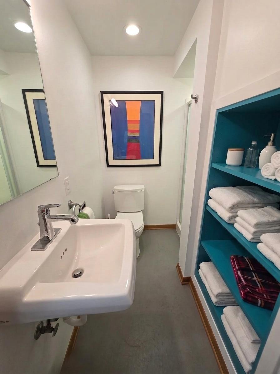 Updated bath featuring a contemporary wall-mounted sink, clean finishes, and colorful custom built-in linen storage.