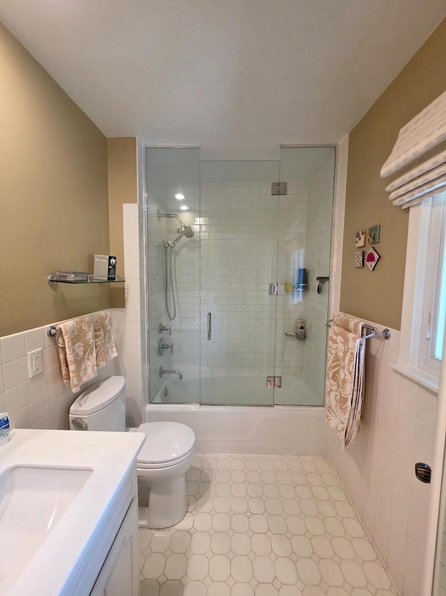 Updated off-suite, full-bath with glass-enclosed tub and shower, crisp white finishes, abundant natural light, and a spacious vanity.