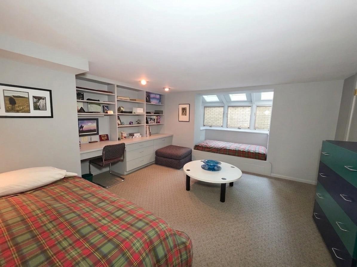 Spacious lower-level bedroom with custom built-in desk, cabinetry, shelving, and a charming window seat surrounded by natural light.