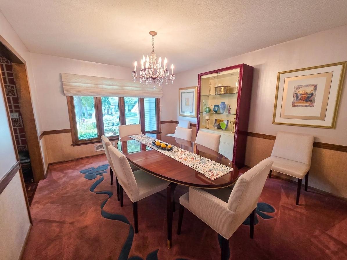 Elegant formal dining room with statement chandelier, rich wood accents, distinctive display cabinetry, and large front-facing windows.